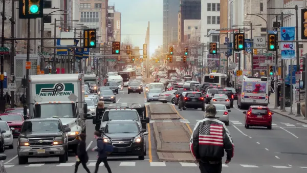 Traffic on street in Philadelphia, Pennsylvania with man wearing jacket with American flag on back in foreground.