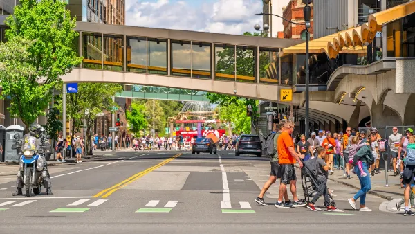People walking across crosswalk in downtown Spokane, Washington with enclosed glass skyway connecting two buildings in background.