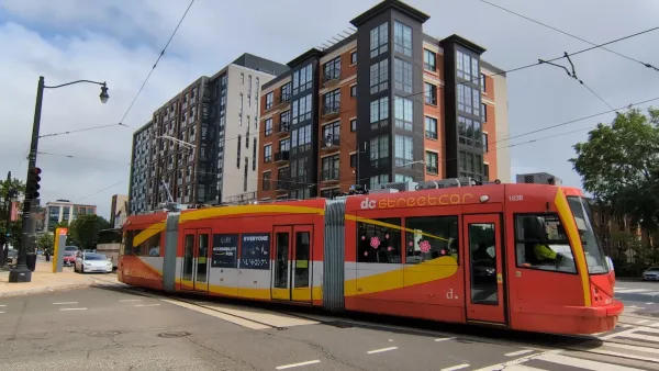 Red and yellow DC streetcar with multistory apartment building in background.