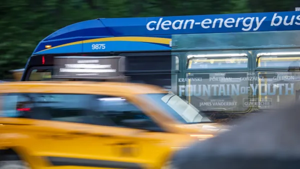 Blue :clean energy" bus blurred passing on city street.