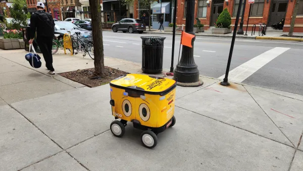 Yellow food delivery robot with cartoonish eyes on side rolling down sidewalk in Chicago, Illinois.