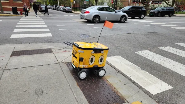 Yellow delivery robot rolling across curb cut onto painted crosswalk.