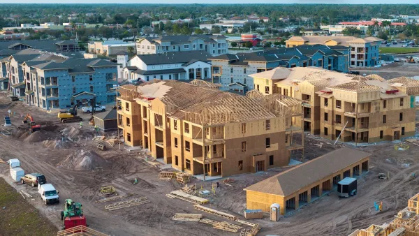 Aerial of three-story wood-frame residential buildings under construction with work trucks around them.