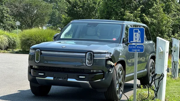 Dark grey Rivian truck plugged into roadside EV charging station.