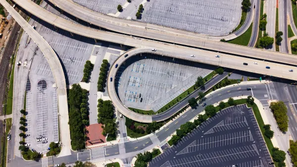 Aerial of wide freeway overpasses over large mostly vacant asphalt parking lots.