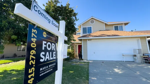 Close-up on For Sale sign in front of yellow house with white garage door.