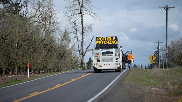 Road repair crew with sign reading 'Pothole Repair' on road.