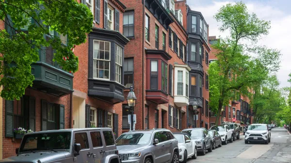 Line of cars parked curbside next to three-story brick homes with bay windows in Boston, Massachusetts.