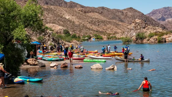 People swimming near shore with parked kayaks on Colorado River beach in Arizona.