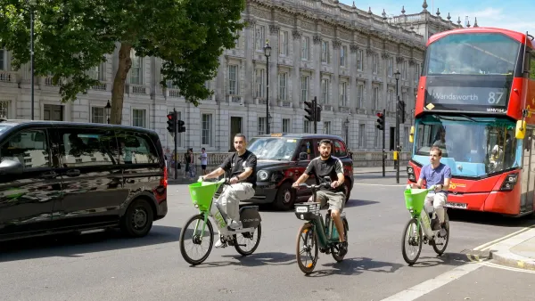 Three people ride green bike share bikes on London street in front of red double-decker bus.