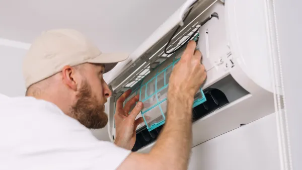 Man installing or repairing mini split air conditioning unit on white wall.