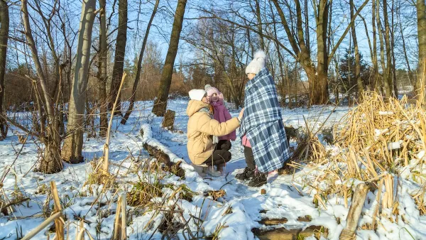 A woman in the snowy woods wraps two children in blankets.