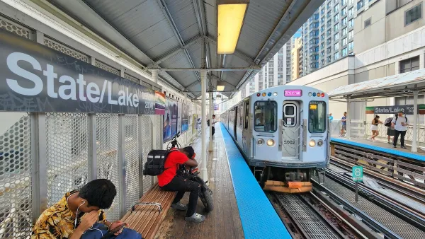 Male passengers sit on wood bench at State and Lake Elevated Train Station with train approaching in Chicago.