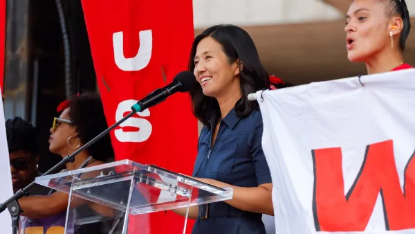 Boston Mayor Michelle Wu smiles behind a glass podium.