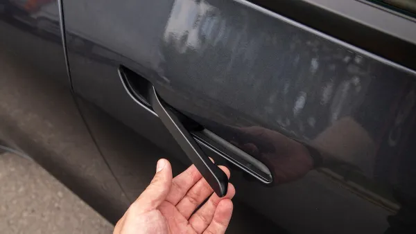 Close-up of hand pulling car door handle on dark grey Tesla.