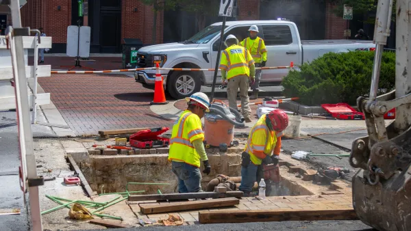 Construction workers in yellow vests stand in a hole in a road in Maryland.