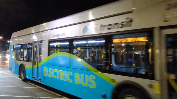 Silver and blue electric transit bus with "Electric Bus" green text moving at night in New Haven, Connecticut.