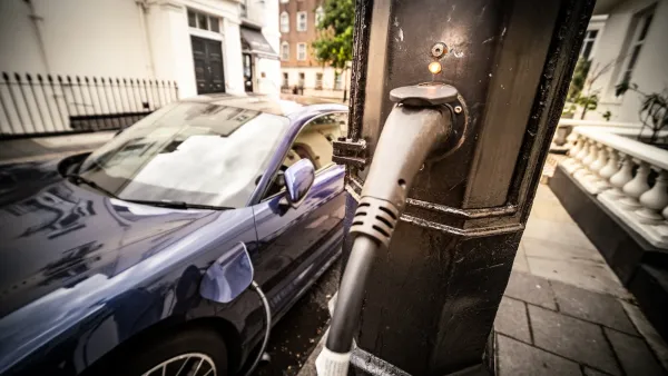 Close-up on utility pole with EV charger cable running out of it to dark-colored car plugged into it.