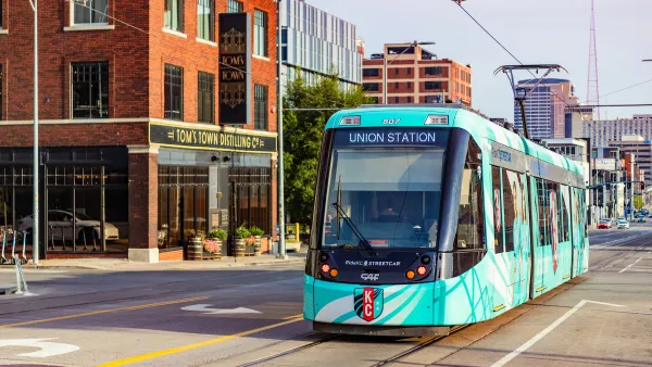 Green Kansas City streetcar driving down street next to brick building with vintage-style 'Tom's Town Distillery' sign.