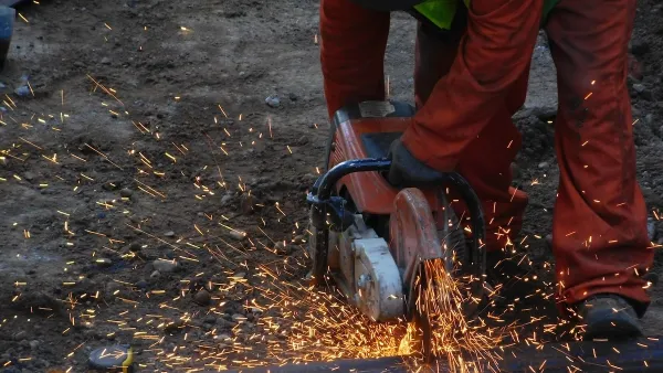 Construction worker uses a power saw to cut through metal.