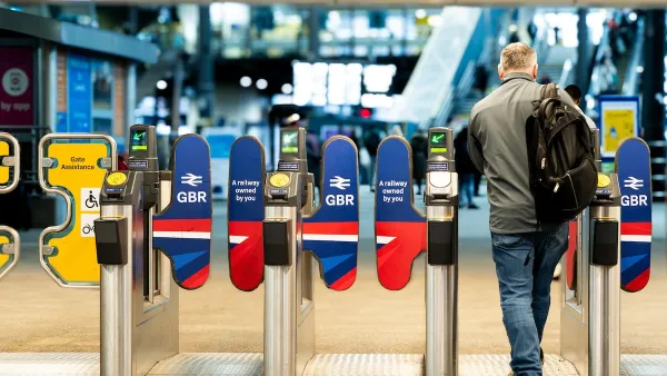 A rail passenger going through the ticket barrier at Leeds Train Station with the UK Government's re-nationalised rail company GBR signs and symbols displayed.