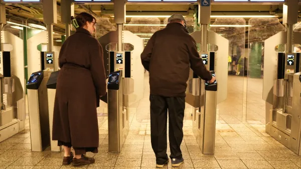 A man and a woman go through NYC's new turnstiles, which are tall, clear double doors.