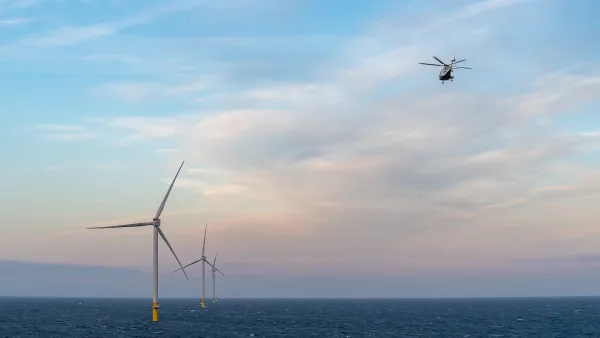 Row of offshore wind turbines in ocean with helicopter flying above.
