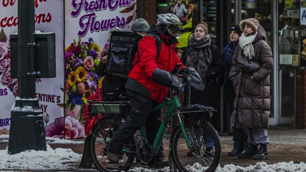 Man in red jacket on e-bike wearing black delivery backpack in winter on New York City street.