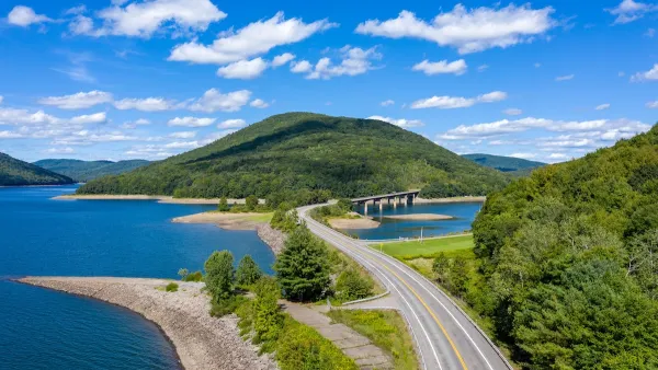 An aerial view of the Cannonsville Reservoir. A road splits in in two, and there are green mountains to the left, and in the background.