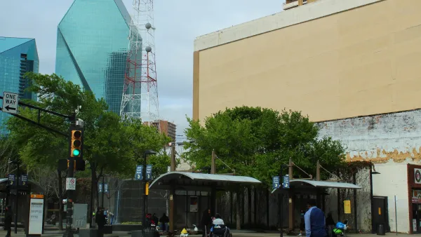 Bus stop with two shelters with benches with modern glass skyscraper with pointed pyramidal top in downtown Dallas, Texas.