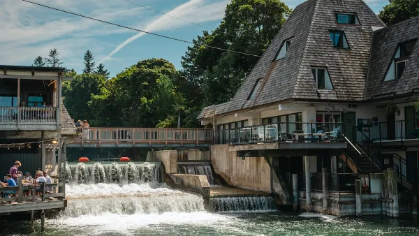 The Leeland Dam, nestled between two buildings with pointed roofs. People watch the water.