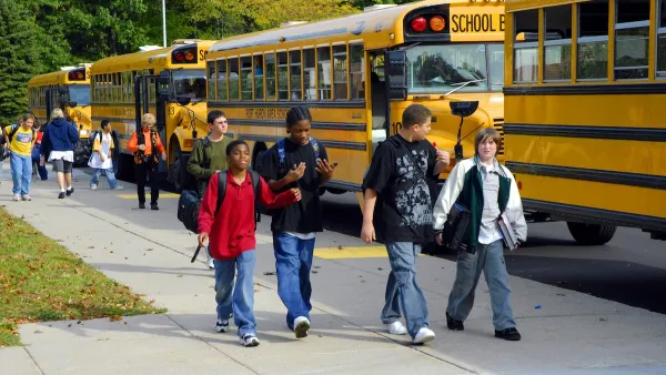 A group of children walk past yellow school buses on the way to school.