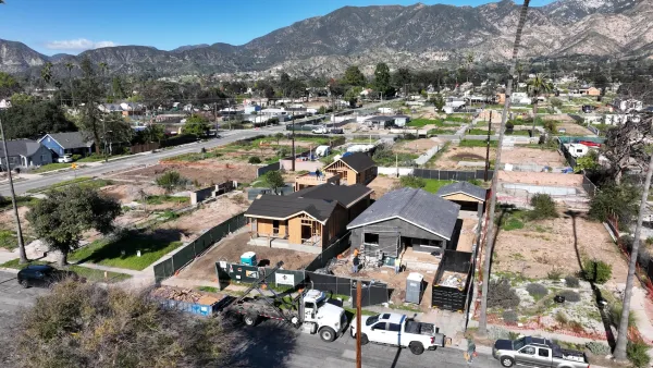 Aerial of two homes under reconstruction in fire-damaged area of Altadena, California with mountains in background.