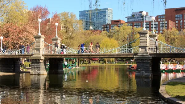 People crossing a bridge in Boston with fall leaves in the background.