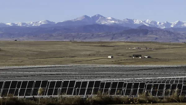 Solar panels n a field with Rocky Mountans visible in background.