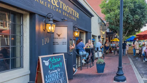 People sitting at outdoor seating tables with umbrellas on commercial street with red brick sidewalk in Bentonville, Arkansas.