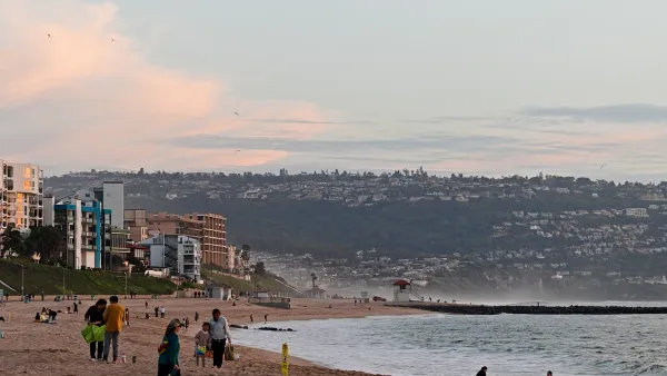 A crowd of people play in the sand at a California beach at sunset.