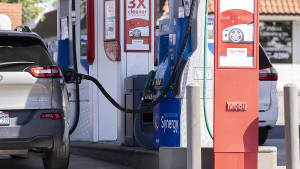 Silver car parked at gas station with gas pump fueling it with no owner there.