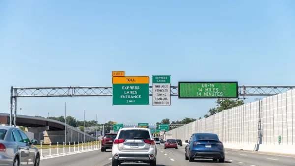 Sparse traffic on freeway with green and yellow signs for upcoming toll lanes.