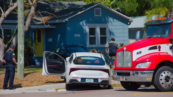 White car with Florida plate Crashed into black car on a suburban lawn with fire truck on the left.