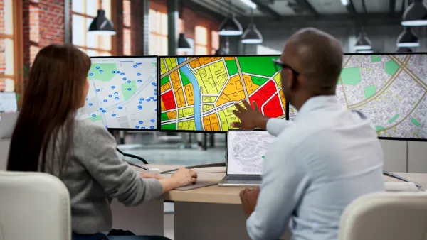 Two professionals sitting at desk with three-monitor computer showing zoning and other maps.