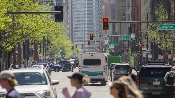 Pedestrians crossing a crosswalk with city traffic and bus in ackground in Denver, Colorado.
