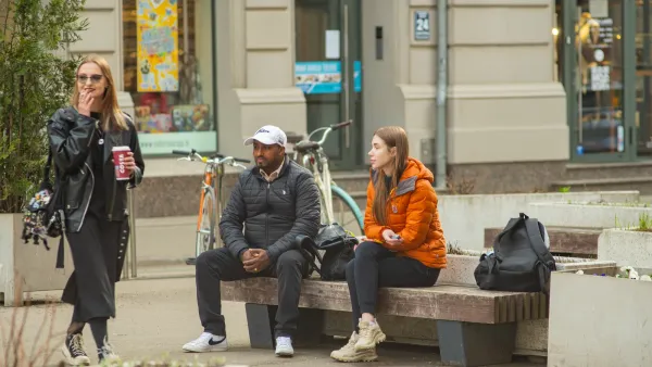 Man and woman sitting on public bench on busy street in Riga, Latvia.