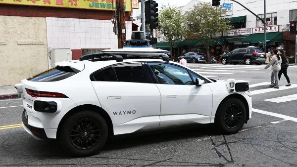 A white Waymo self-driving car at an intersection in Chinatown, Los Angeles.