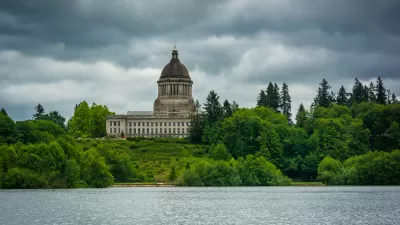 View of Washington state capitol building dome from across lake with green trees in foreground and grey cloudy sky