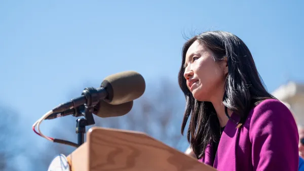 Mayor Wu speaks behind a wooden podium. She has black hair slightly past her shoulders and is wearing a magenta jacket. 