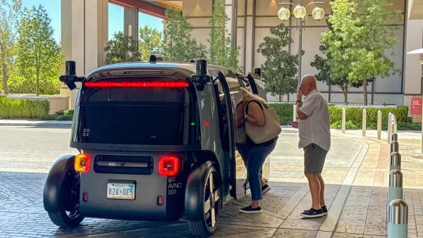 Older couple boarding dark grey Amazon Zoox self-driving pod.