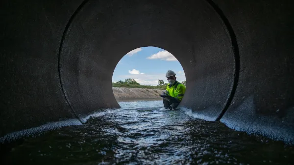 A person in a bright green jacket stares down a culvert, a pipe meant to divert rainwater from roads. 