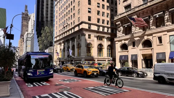 A bus lane with a bus driving on it and a person biking. Parallel, people drive cars down a busy street.