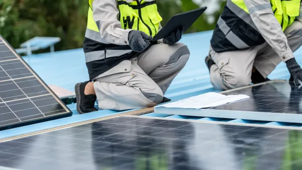 Two people in hi-vis vests install solar panels on a blue roof.